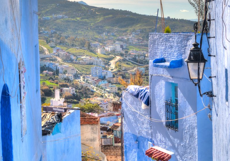 A narrow blue alley in the Chefchaouen medina with the mountains behind