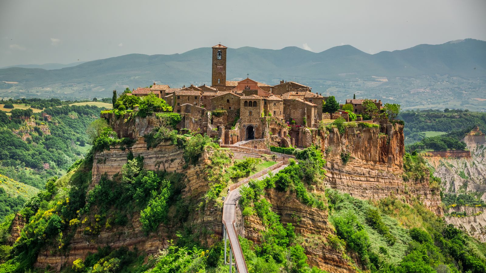 Civita di Bagnoregio on its eroding hilltop above a green valley, with the long footbridge leading up