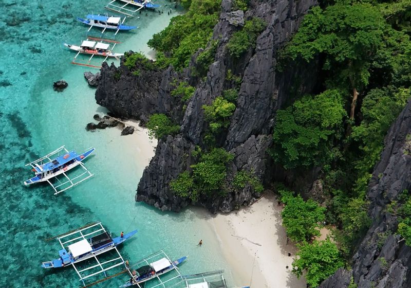 Boats anchored off a white beach below limestone cliffs